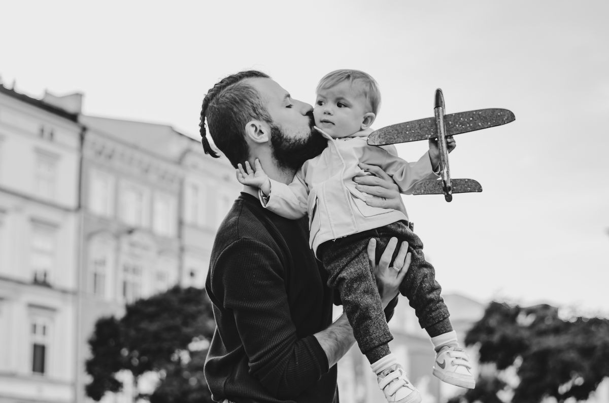 The father plays with the child in his arms by a toy plane in the middle of the tourist center of the old town in Poland.